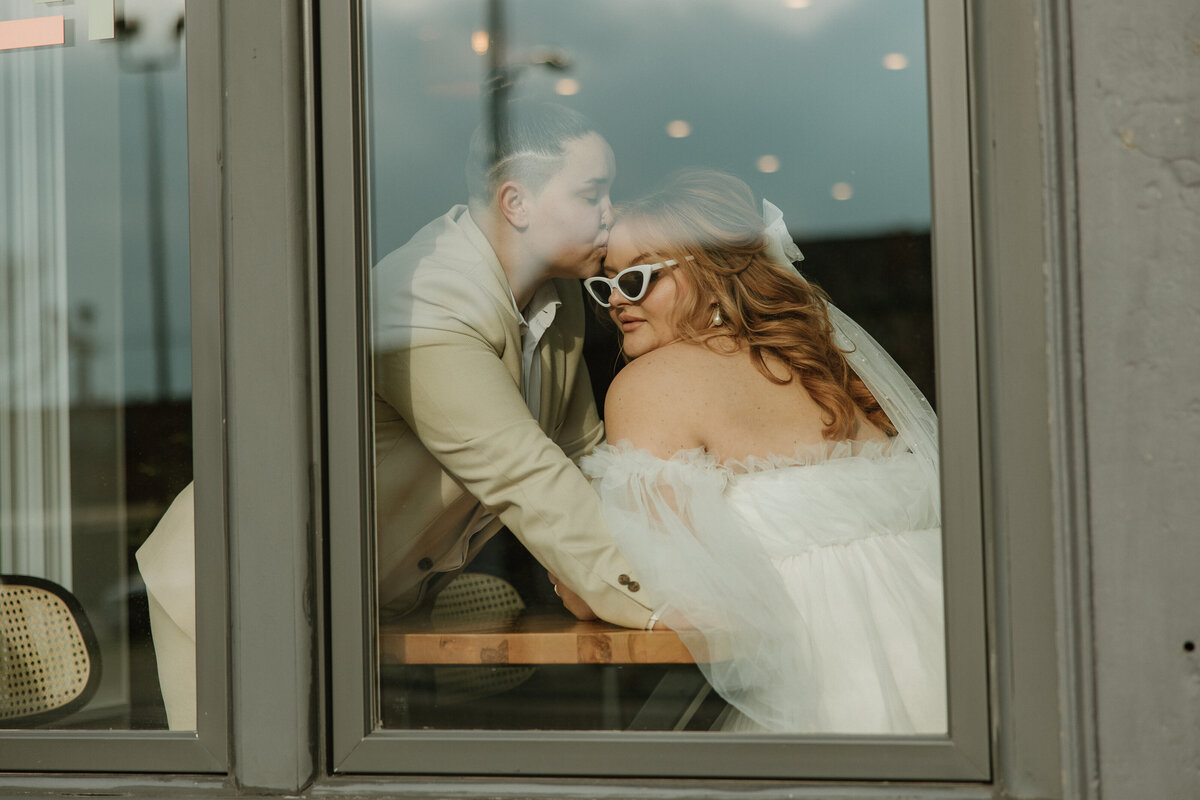 a lesbian couple kisses through the window of a store