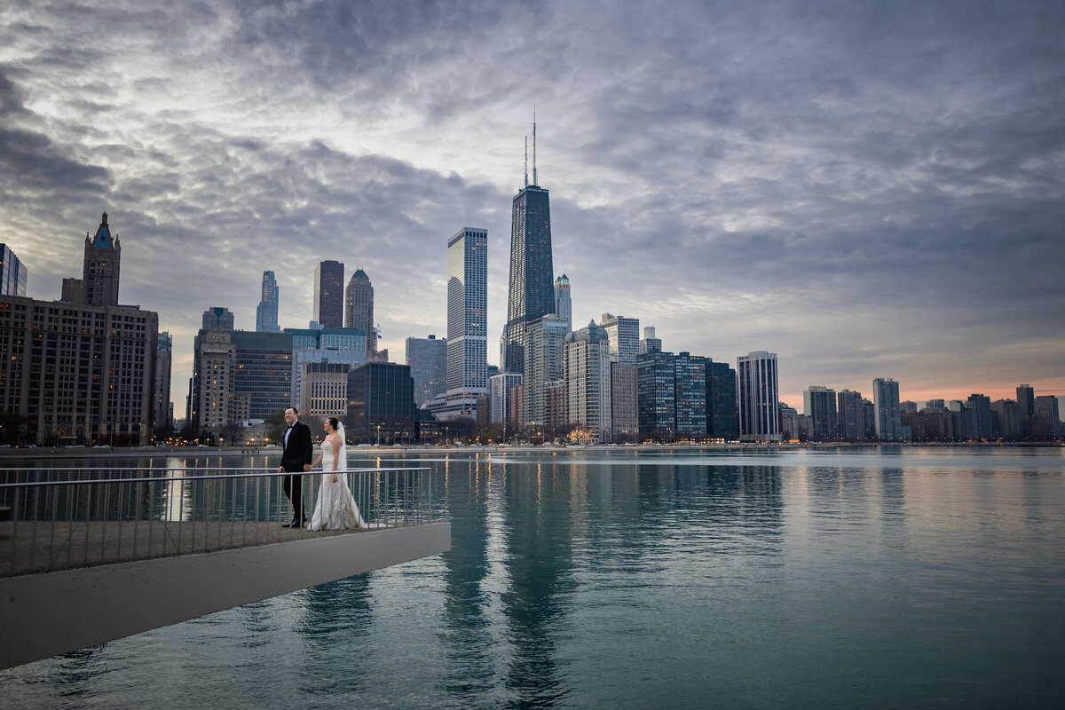 Sunset Bride and groom walk next to Lake Michigan with the Chicago skyline as a backdrop at the Milton Olive Park in Chicago, Illinois