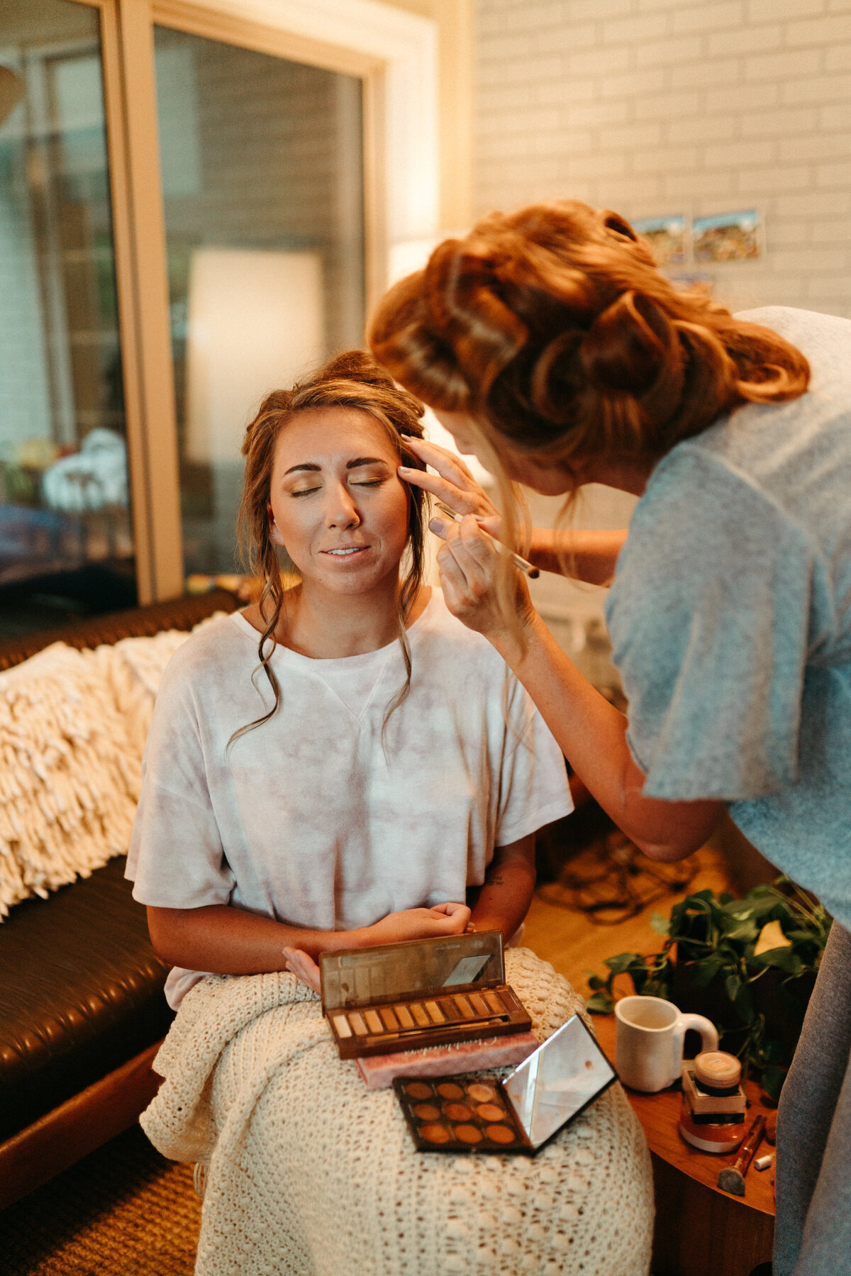 Bride's maid of honor and sister doing her makeup the morning of her wedding