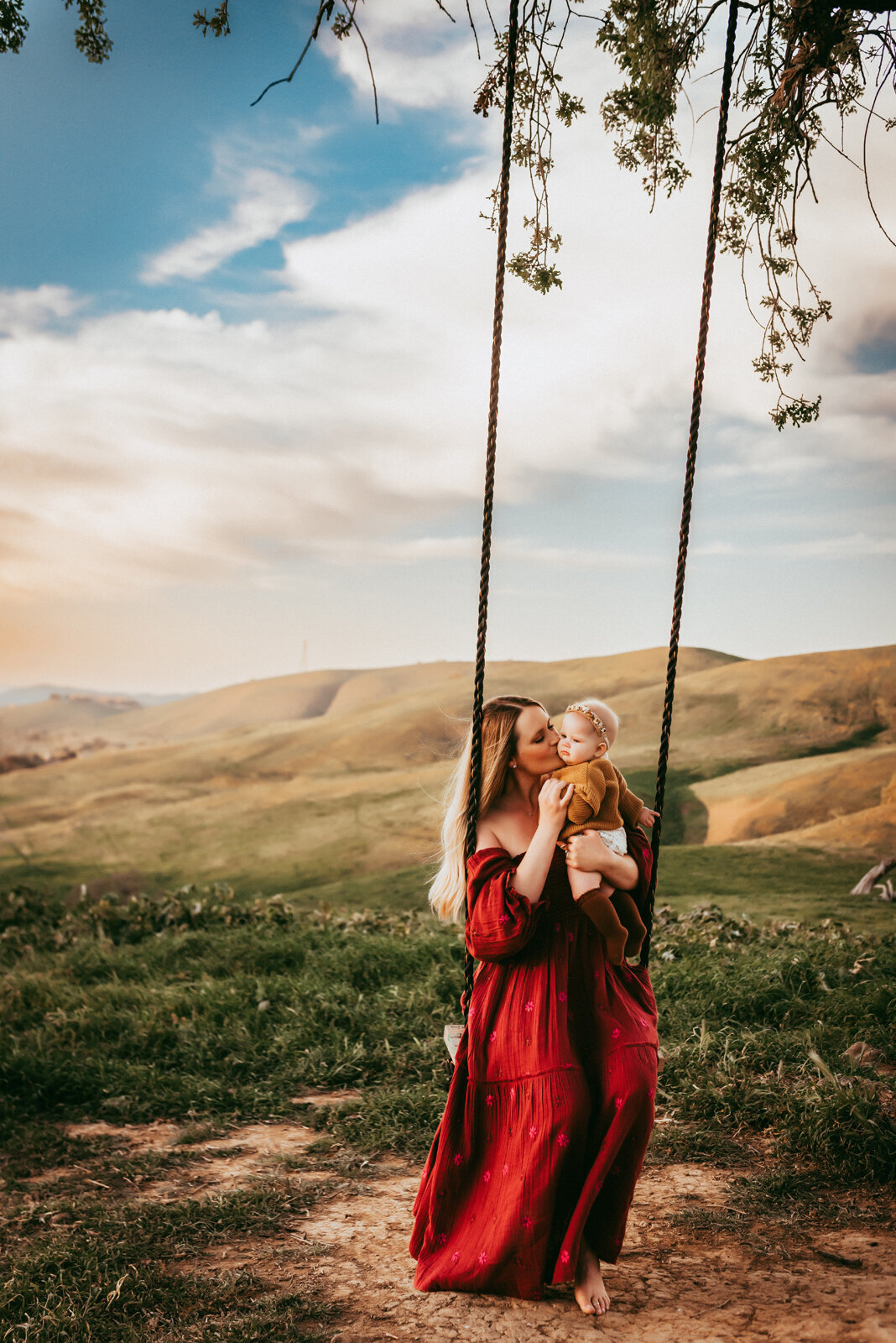 Mama kissing daughter while on a swing in the East Bay Hills