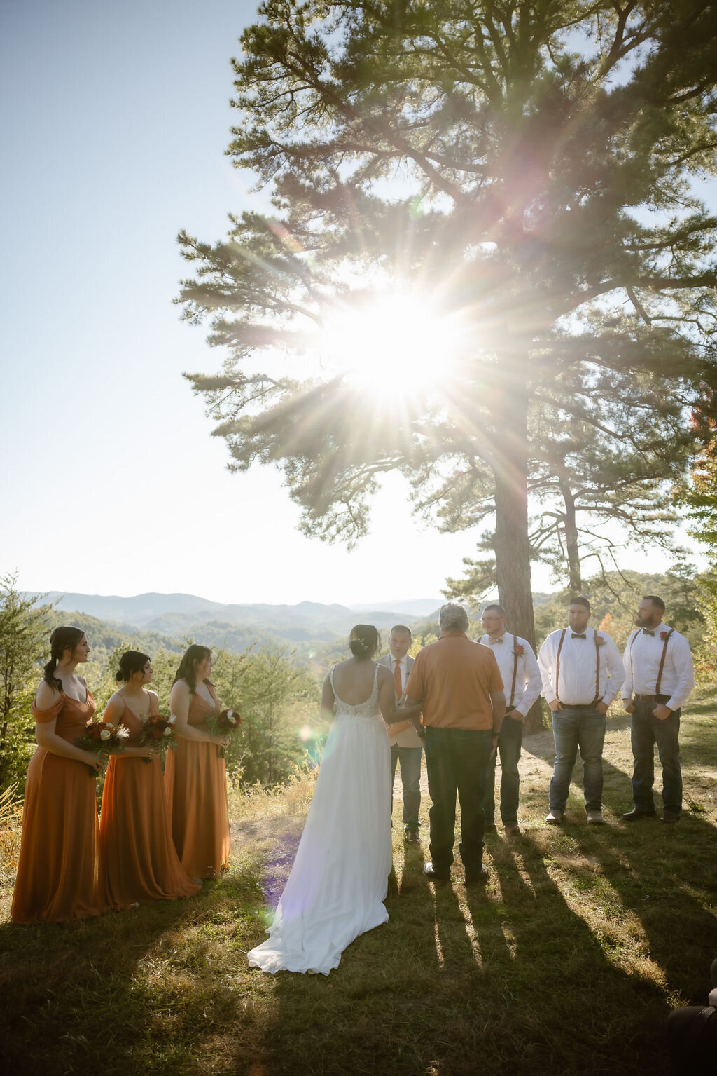 outdoor ceremony at sunset in the Foothills photographed by Gatlinburg photographer with bride and her father walking down the make shift aisle between white folding chairs 
