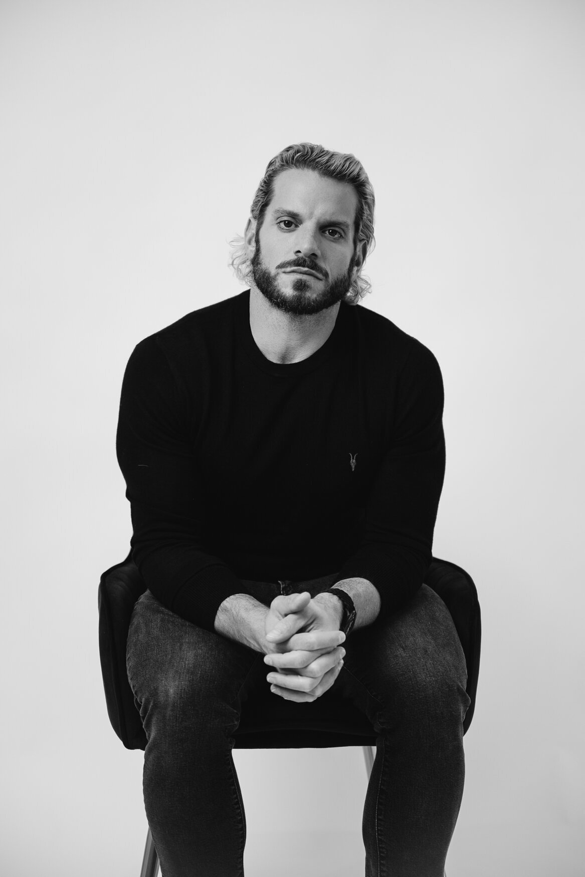 a black and white portrait of a man sitting on a shirt and looking directly to the camera