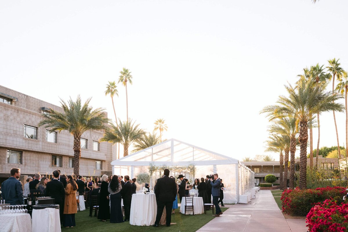 Arizona Biltmore Scottsdale wedding venue during cocktail hour with guests mingling under a clear tent surrounded by palm trees and luxury garden views.