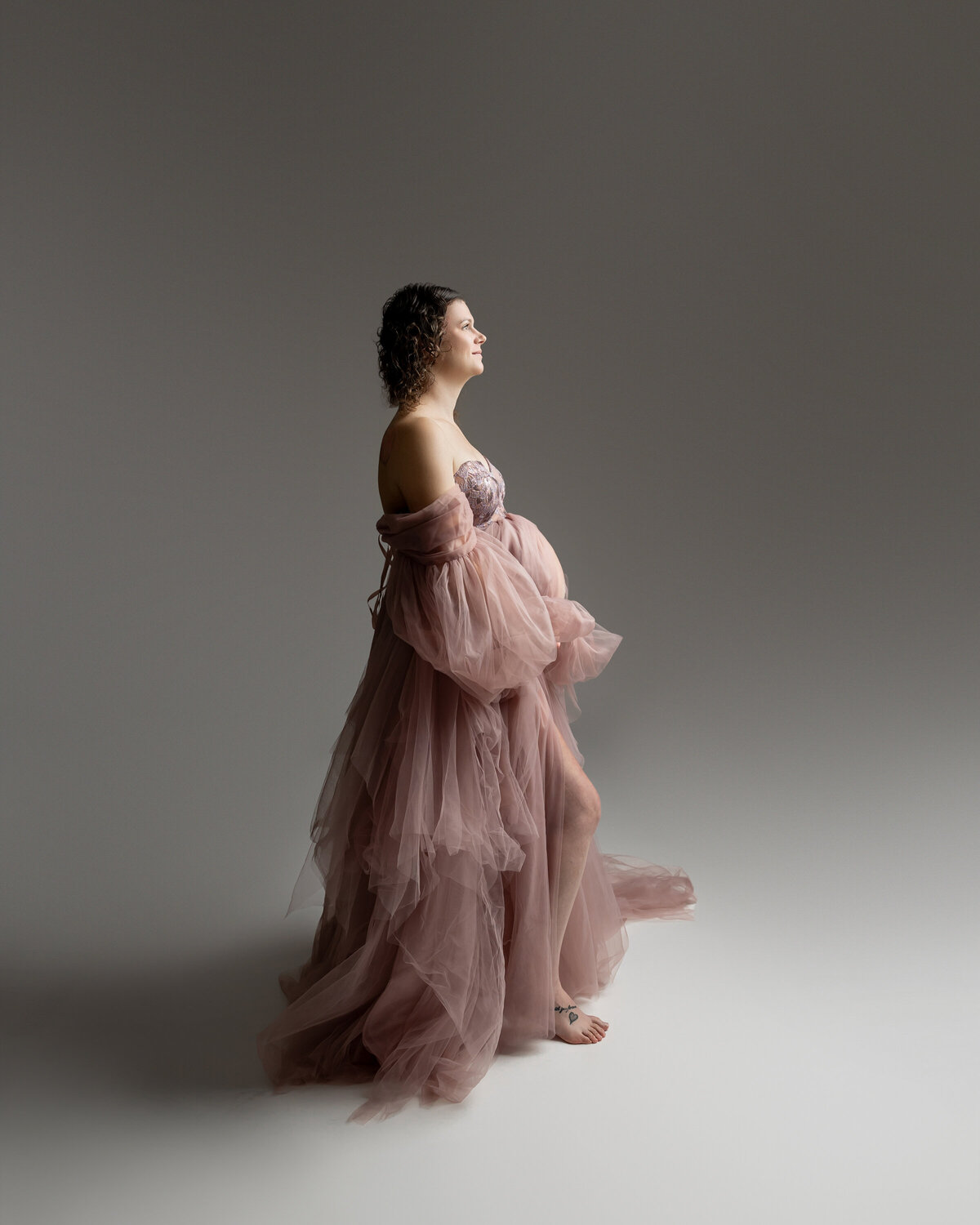 Stunning side profile of a glowing mother-to-be in a black form-fitting gown, showcasing her baby bump against a dark backdrop. Captured in a timeless maternity portrait by Inland Empire maternity photographer Kaitlyn Dawn Photography
