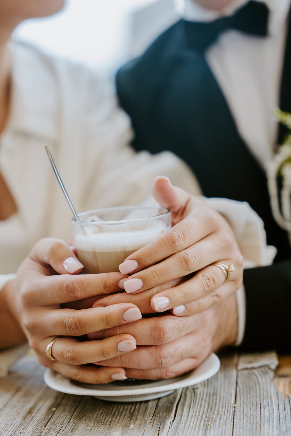 Close-up of bride holding coffee with wedding rings visible.