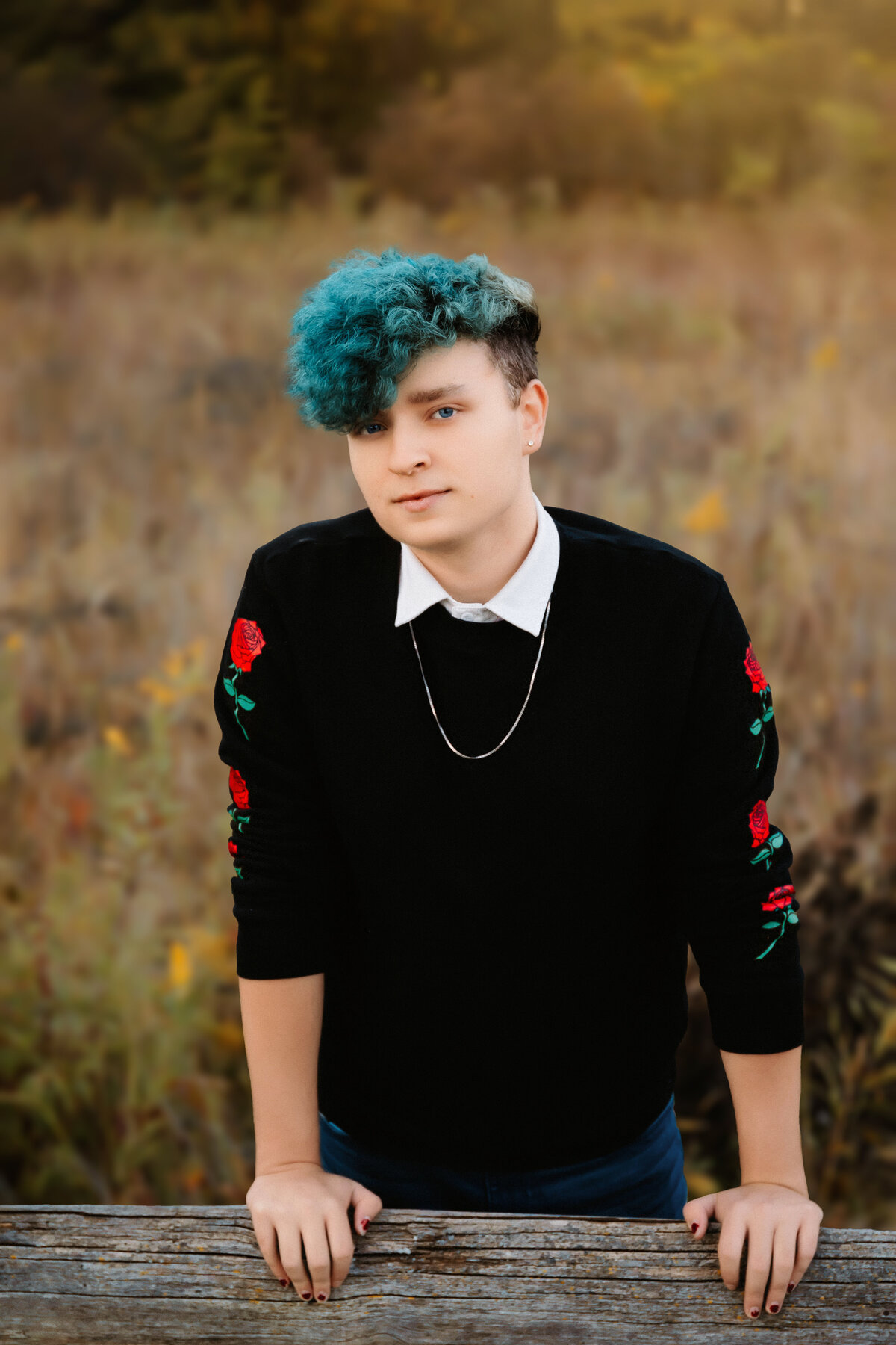This senior poses in front of a wooden fence for his senior photos.