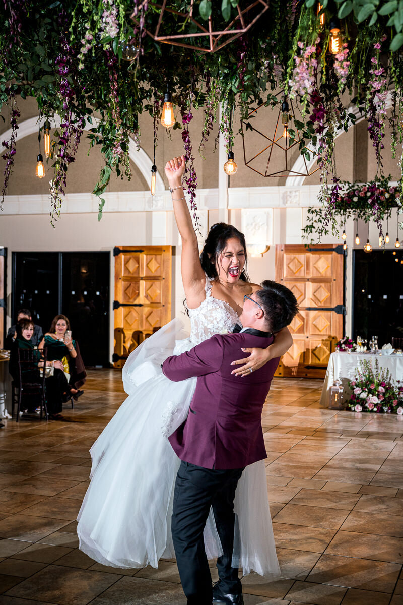 The groom lifts the bride in a celebratory dance move at Casa Real, as she raises her arm in pure joy and excitement, creating a lively and unforgettable moment on the dance floor.