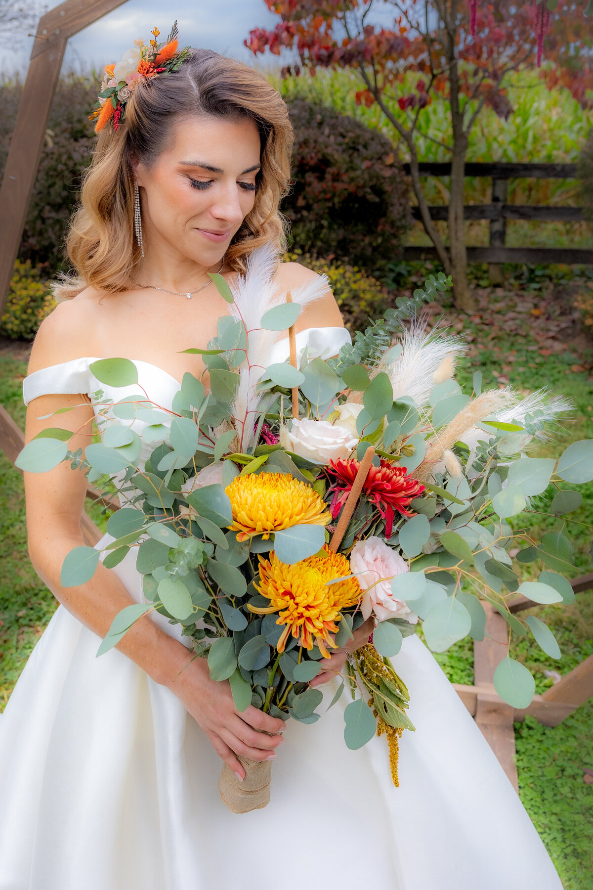 A bride wearing a white dress with autumn flowers in her hair while holding a bouquet of fall blooms