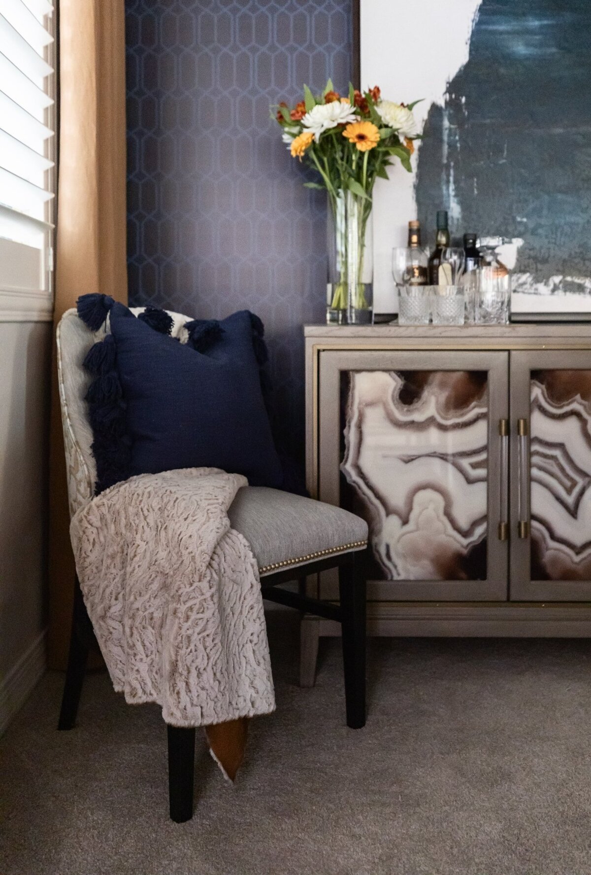 Luxe accent chair with navy pillow and throw beside a modern bar cabinet with agate inlay, styled in a Phoenix living room.