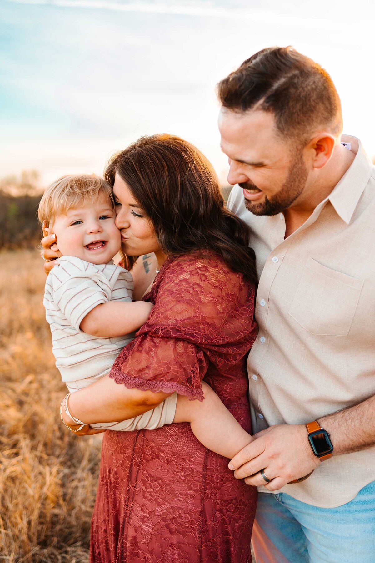 The expert family photographer in Albuquerque captures a heartwarming sunset moment. The mom, dressed in a pink long dress, is lovingly carrying her son as they enjoy a beautiful evening together.