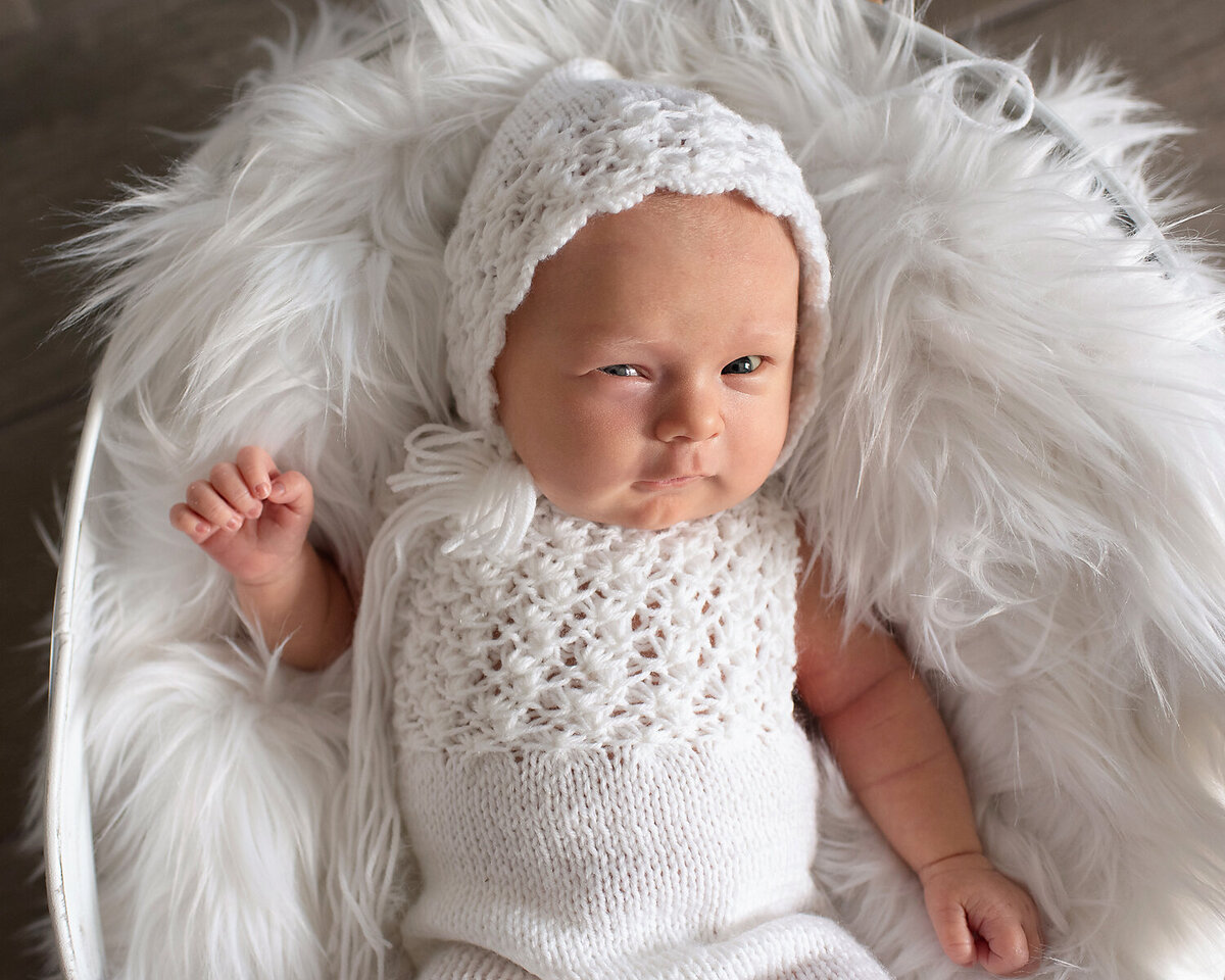 Newborn baby girl in a white romper and matching bonnet at her lifestyle newborn session in Frisco, TX.