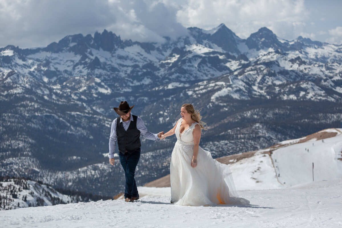 A bride and groom walk up a snowy hill on their wedding day as their California elopement photographer takes their photo.