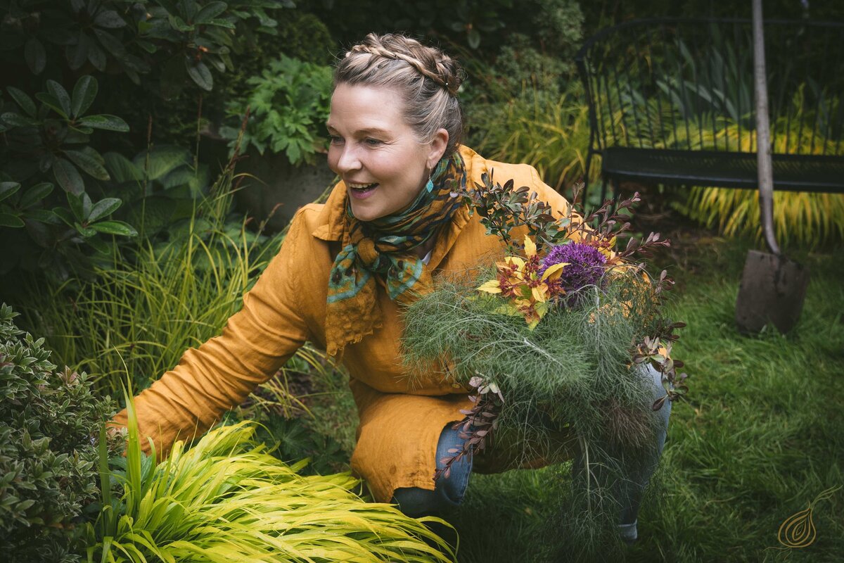 A woman in a kneeling position on the grass, gently holding a bouquet of flowers, enjoying the tranquility of nature.