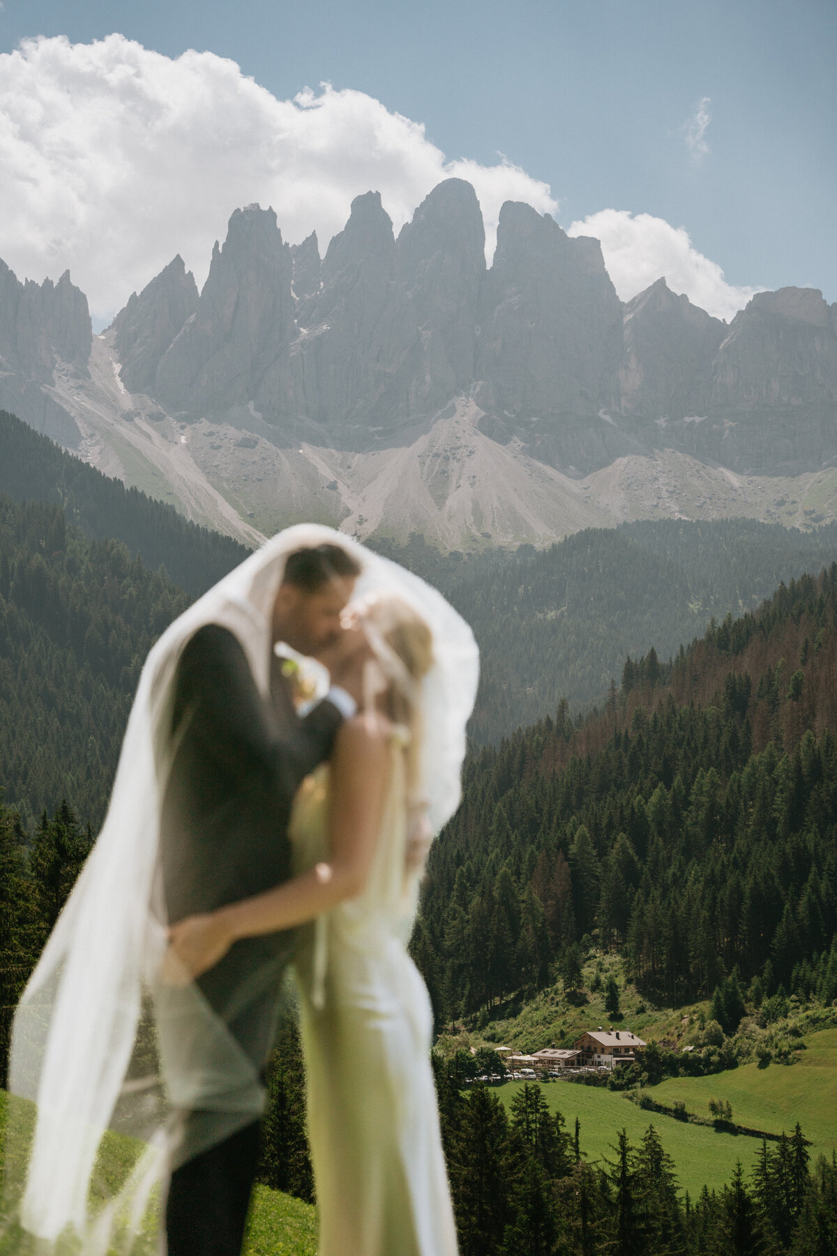 Bride and groom embracing with veil flowing in mountain meadow
