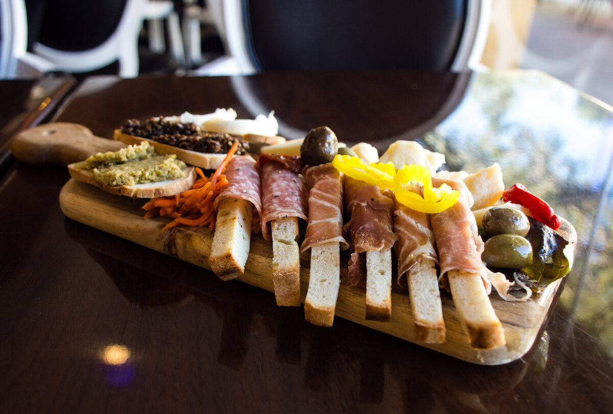 Italian meats, cheeses and spreads on crostini  on a cutting board on a dark wooden table