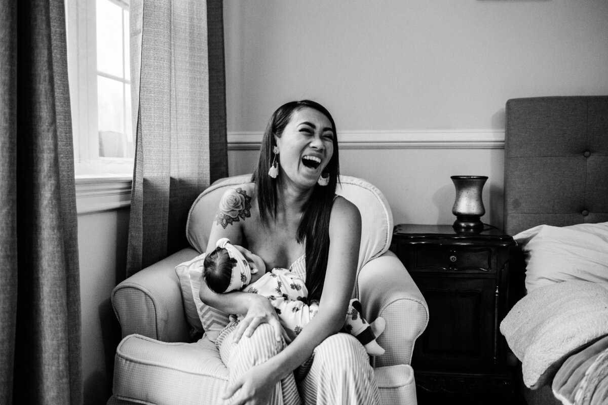 newborn-mom-laughing-holding-baby-nursing-in-home