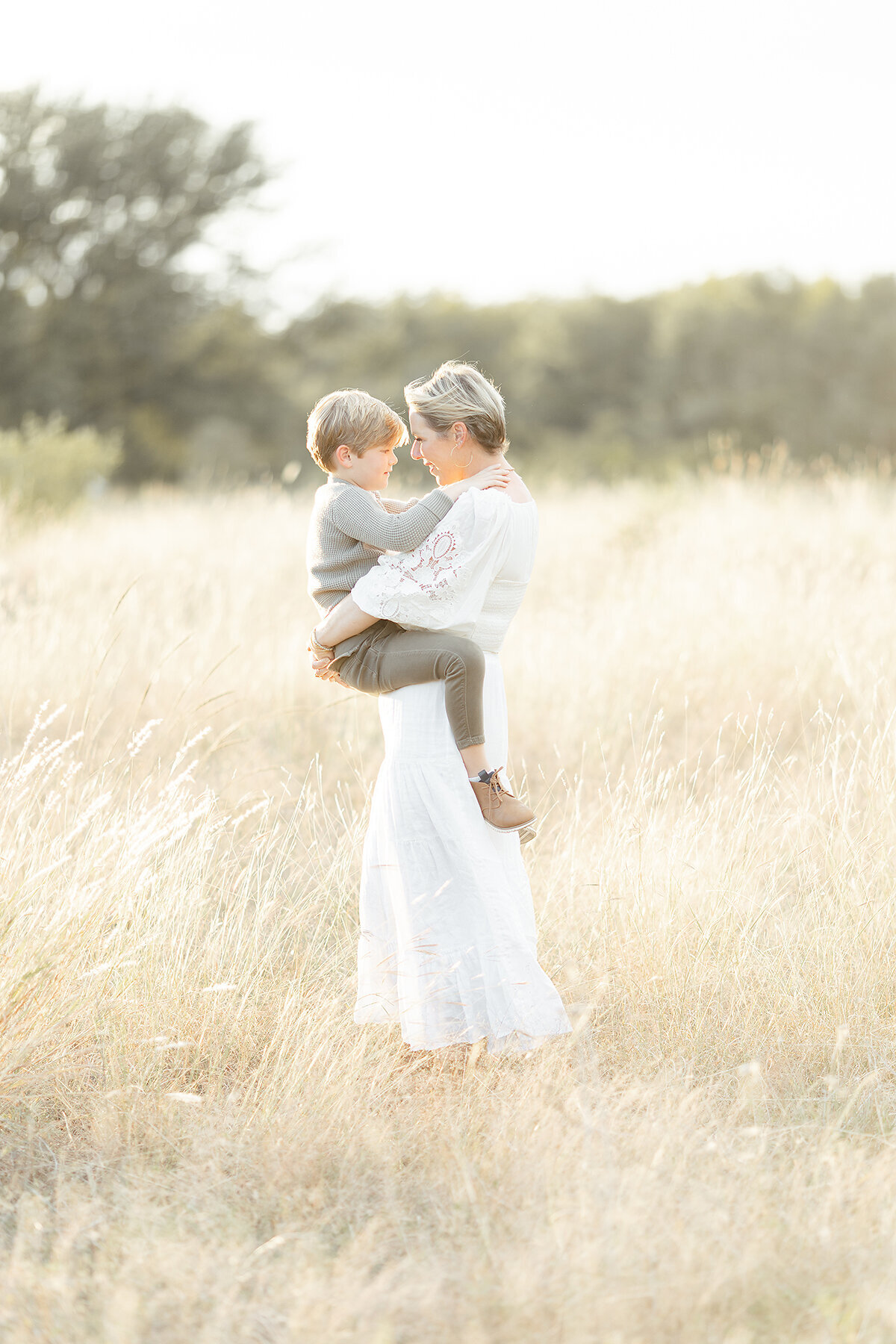 A photo of a mother carrying her son in a grassy field for their family photos.