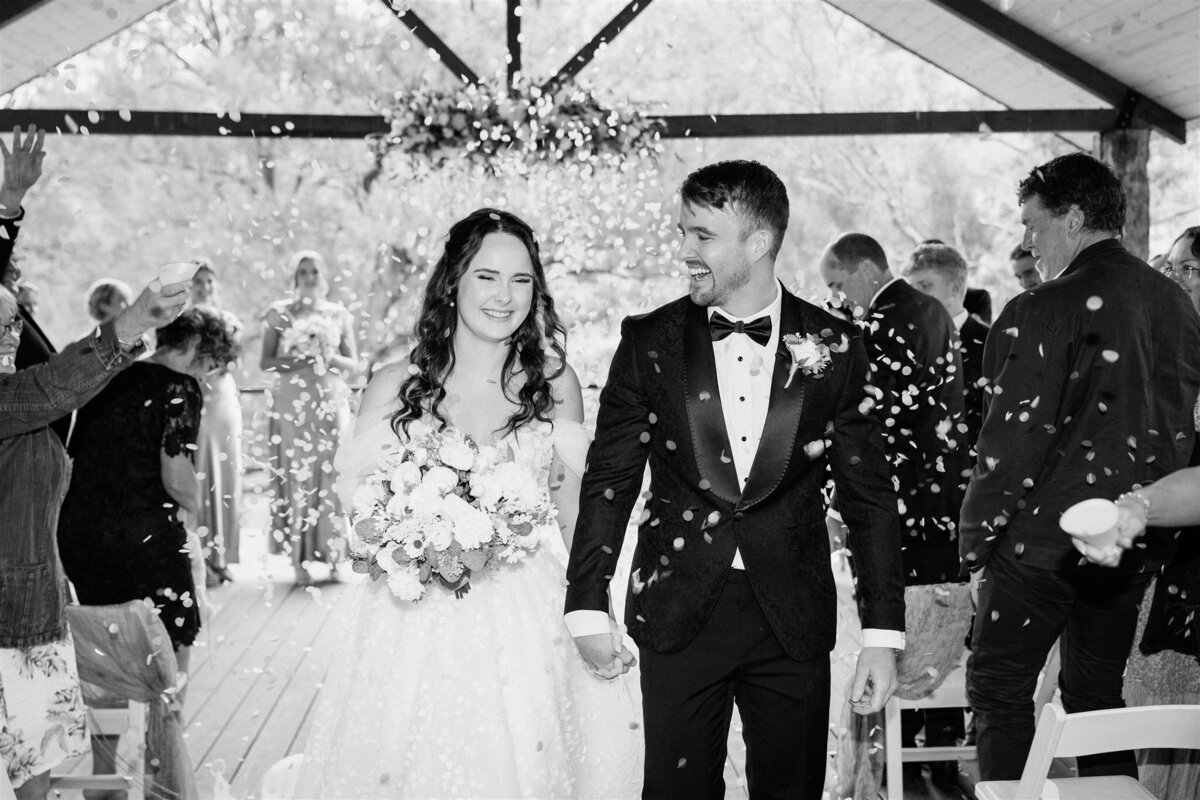 The bride and groom walk hand in hand, bathed in golden sunlight, as they exit the ceremony, their joyous smiles capturing the essence of their newfound union.