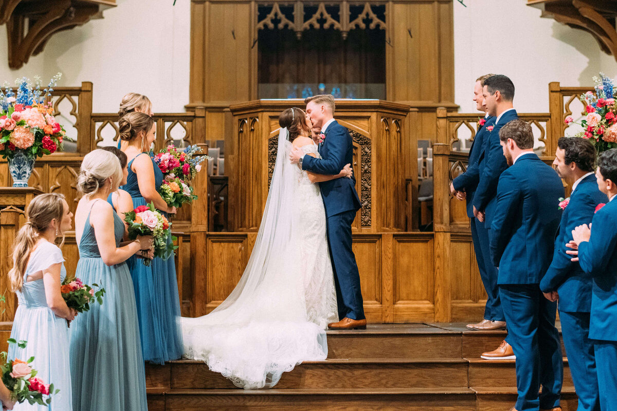 Fort Worth bride and groom kiss at the altar during colorful summer wedding