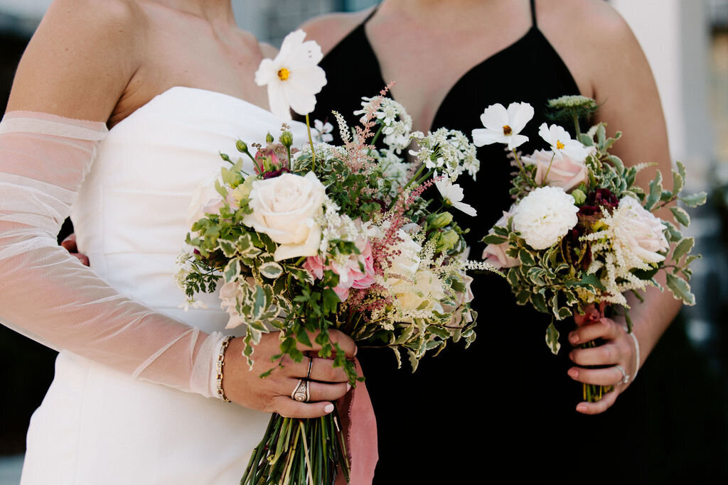 A bride and a bridesmaid in a black dress holding bouquets