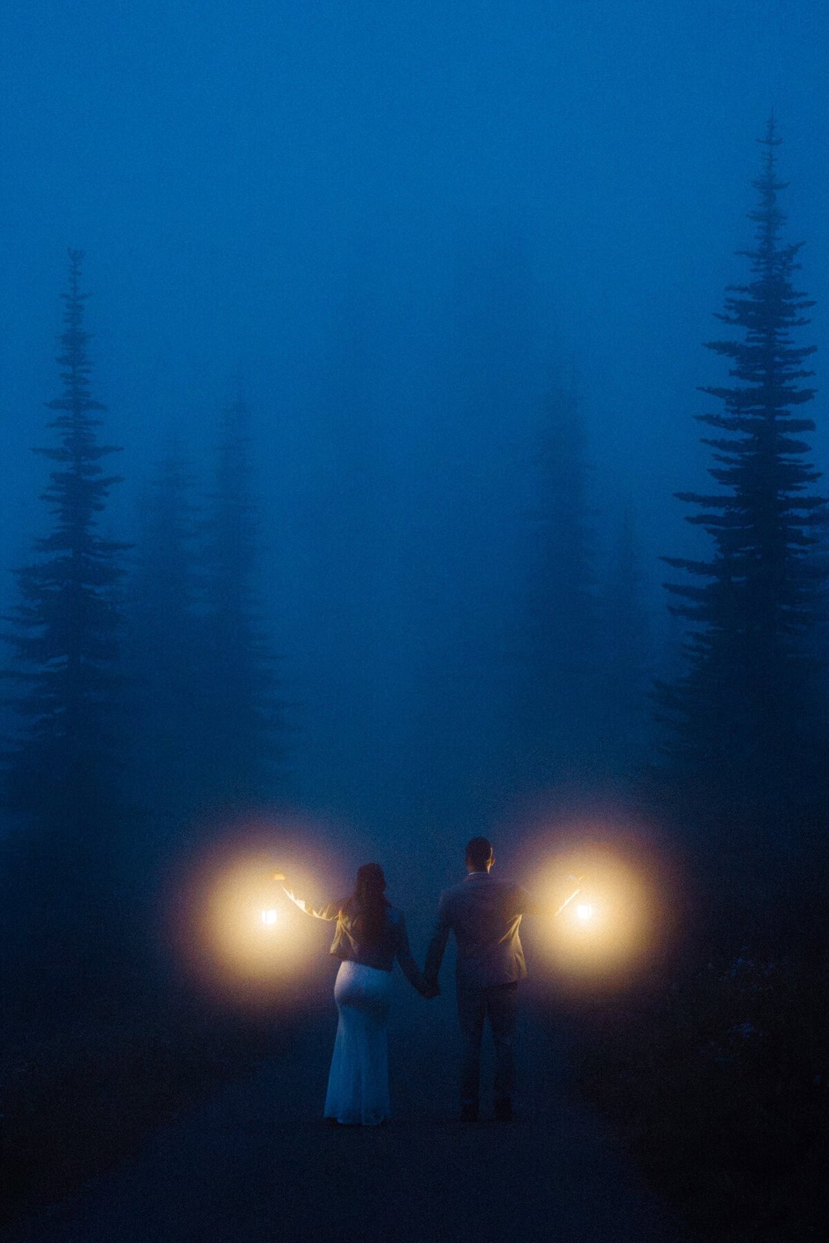 An eloping couple holding lanterns in foggy forest in Mt Rainier National Park after the sun set.
