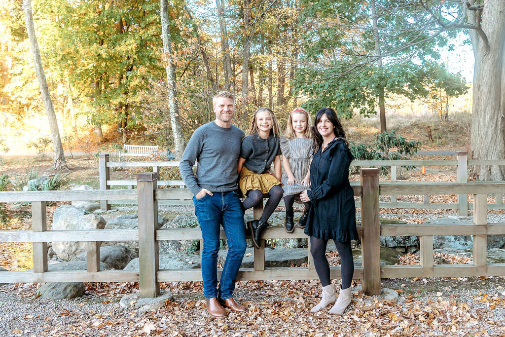 Connecticut family photographer captures family of four sitting on wooden fence during golden hour fall portrait session