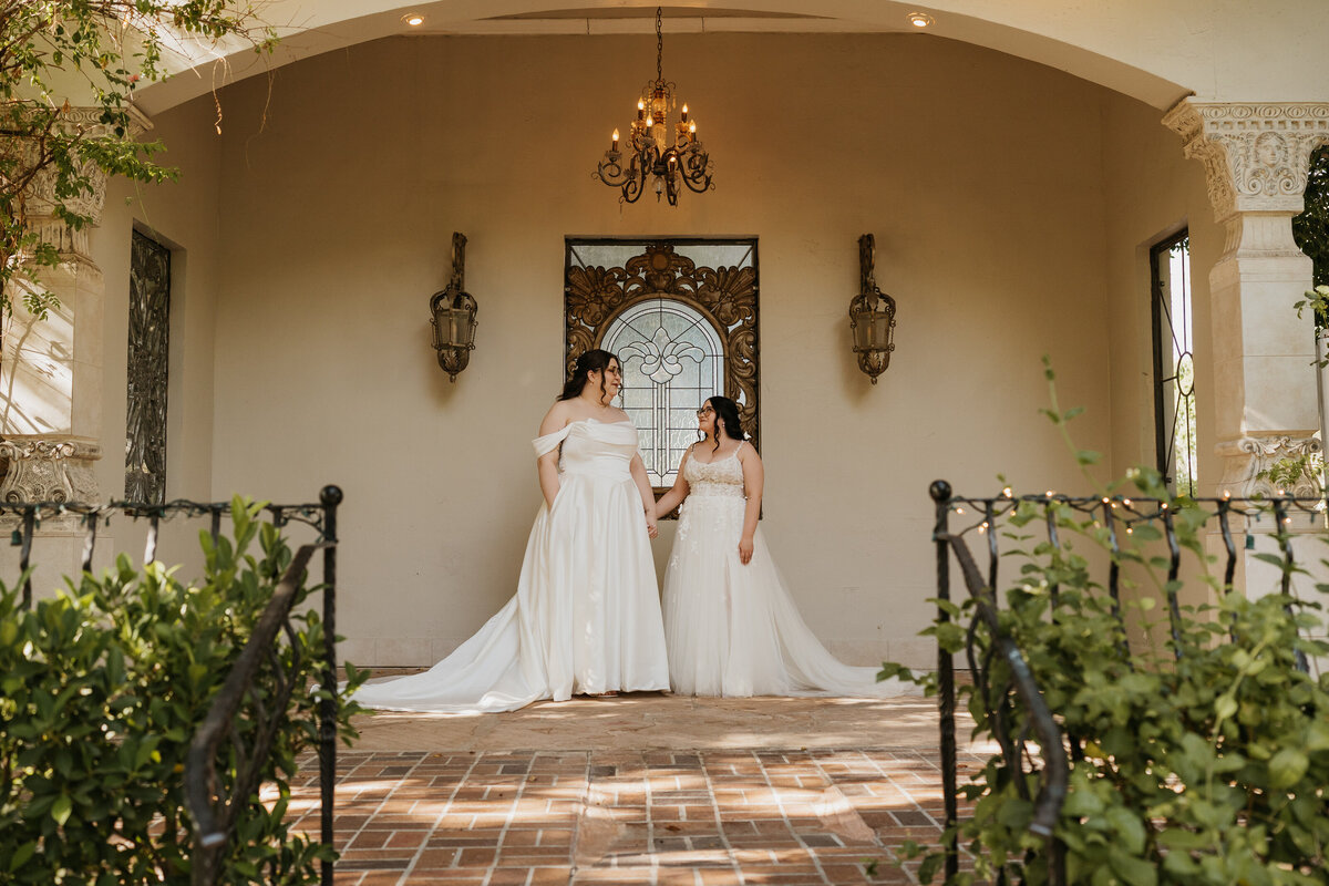 A newlywed couple holding hands and standing in front of a European style building 