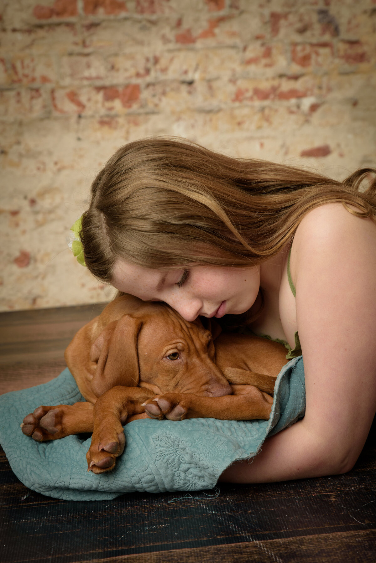 Beautiful young girl wearing a green dress holding her Vizsla puppy in front of a brick background at my home studio near Green Bay, Wisconsin.