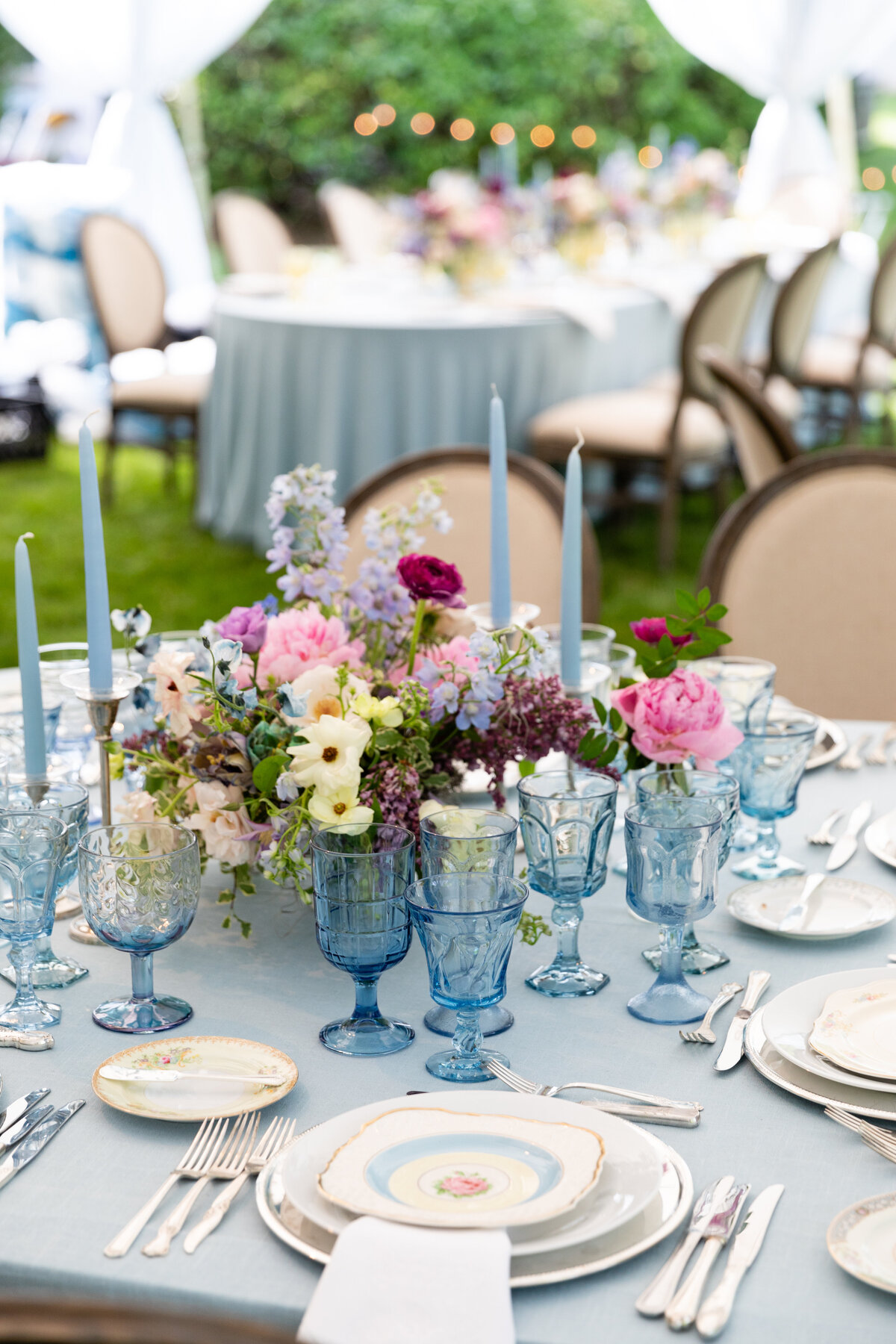 Growing, fresh floral centerpieces with blush garden roses, lilac, blue sweet peas, ranunculus, lavender delphinium, globe allium, and natural greenery for a tented Bridgerton inspired engagement party at a private home in Nashville, TN. Flower by Te