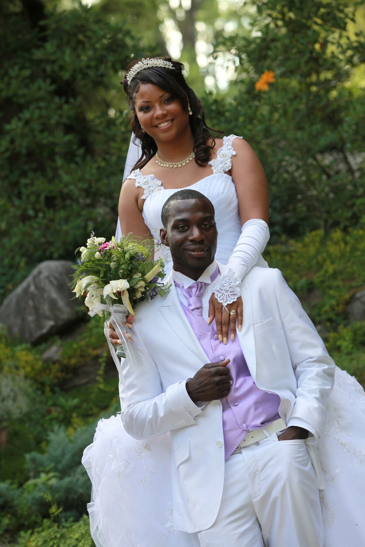 The bride stands gracefully behind the groom, with her arms wrapped around him. The image highlights a loving and supportive pose, showcasing the couple's intimate connection.