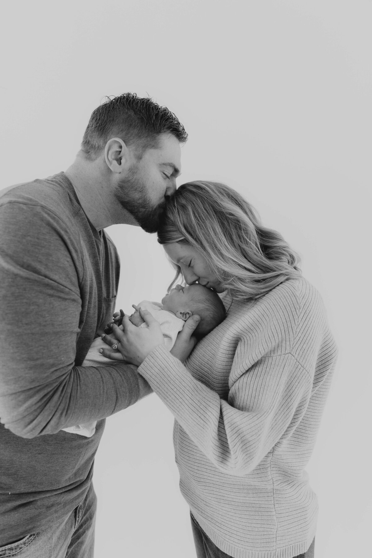 Parents cradling newborn in cozy indoor session, natural newborn photography in Ohio for families seeking emotional, connection-driven portraits
