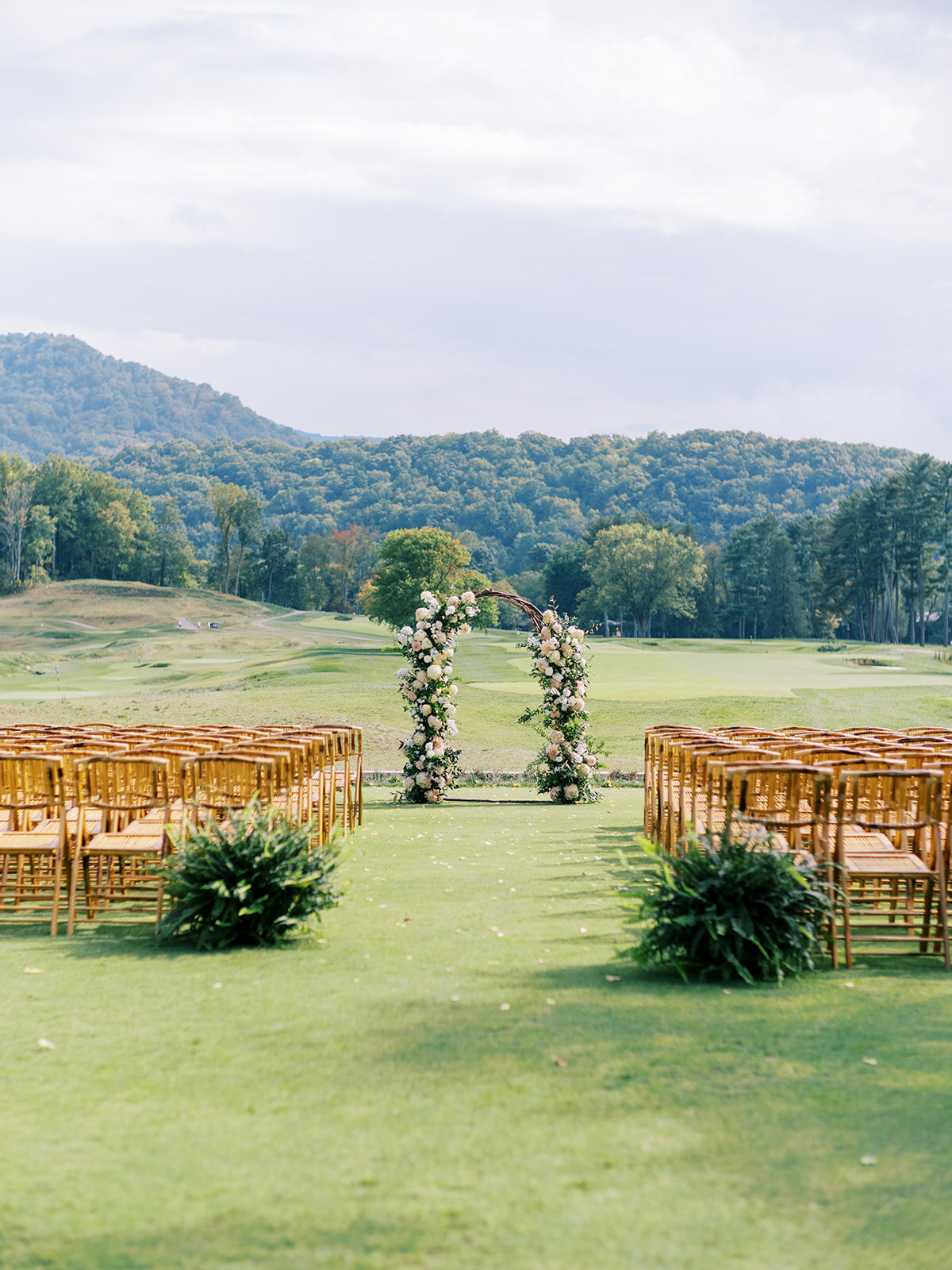 Outdoor ceremony setup with floral arch and wooden chairs overlooking mountain views at The Waynesville Inn & Golf Club wedding in Waynesville, NC.
