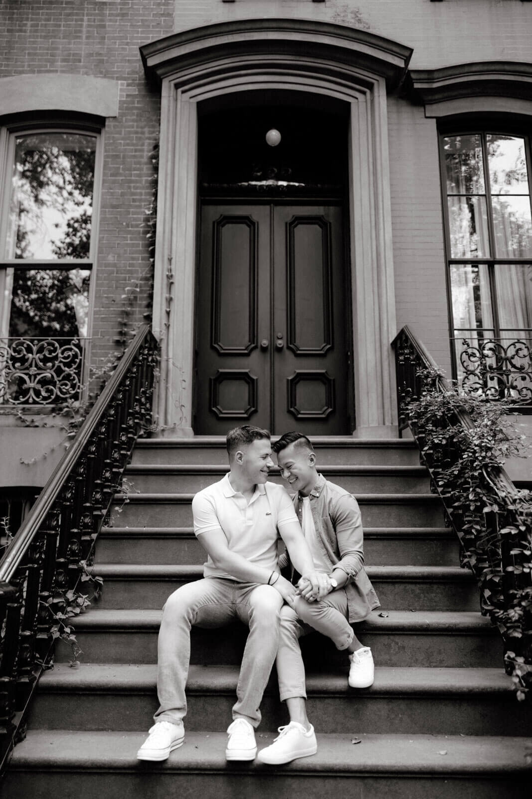 Black and white photo of the engaged couple sitting in a staircase of an ivy-covered building at West Village, NYC.