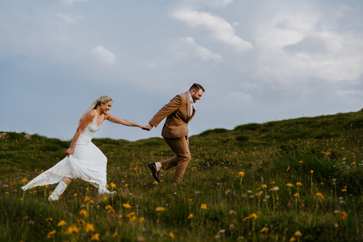 Bride and groom running across grassy hillside at Passo Giau