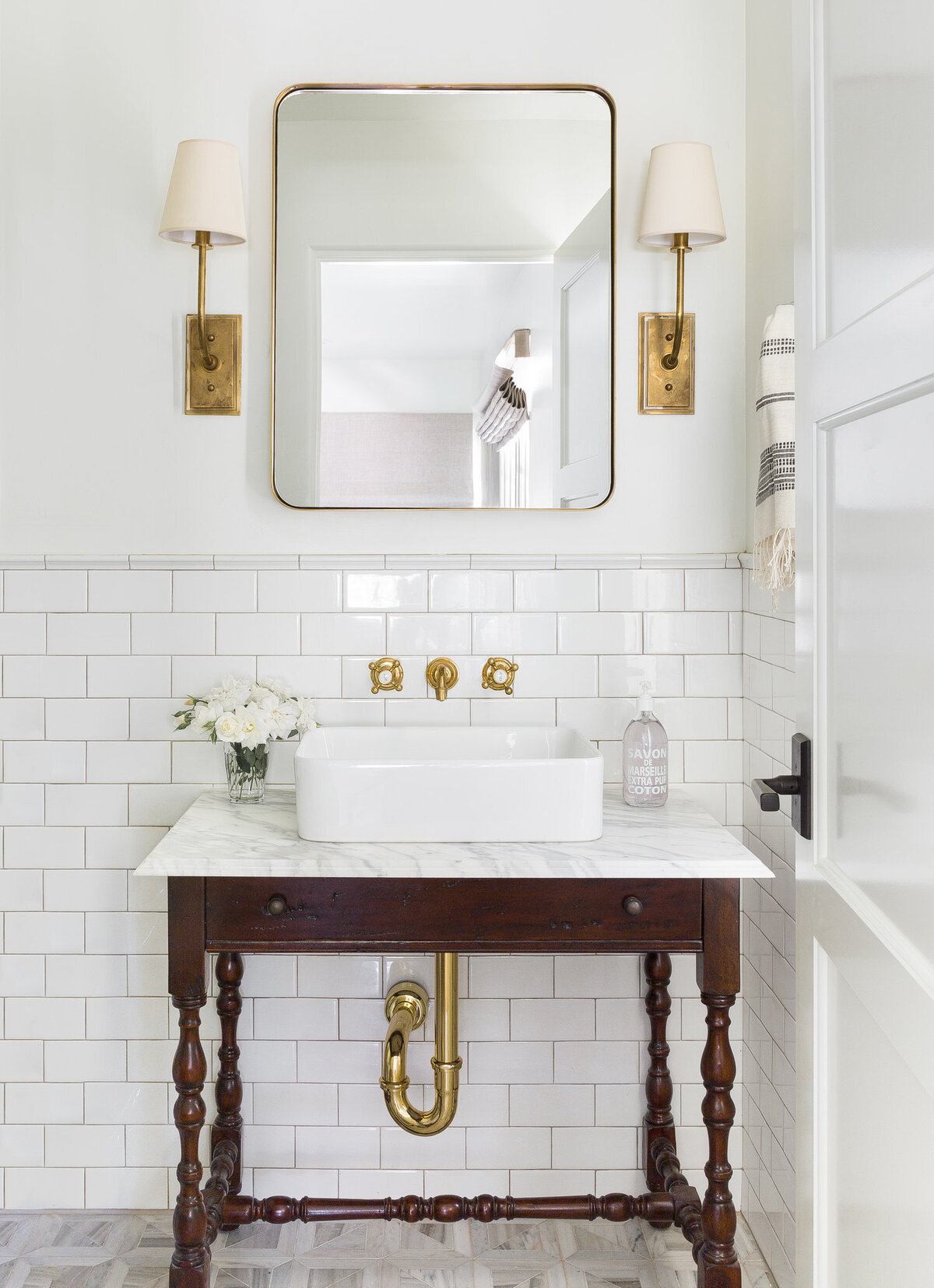 Bathroom-with-wooden-converted-vanity-subway-tile-walls-brass-sconces