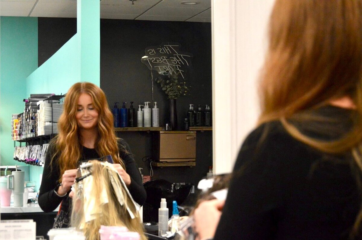 A hairstylist preparing foils for a highlighting session, smiling while working in the salon, showcasing the detailed and friendly service at 212 Salon, Spa, & Barbershop.