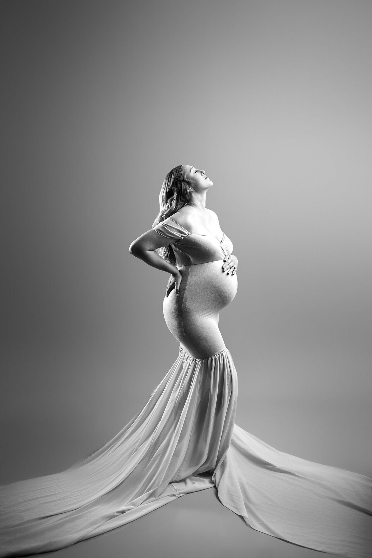 Black and white modern maternity portraiture using dramatic lighting and poses to show off pregnant belly