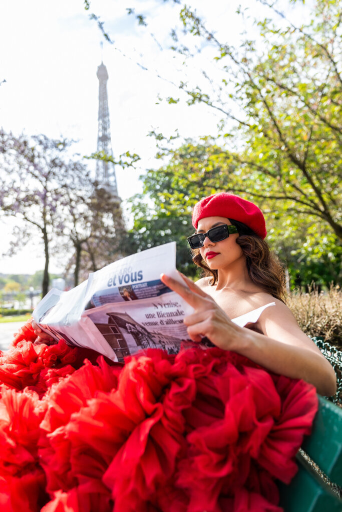 Lifestyle Paris portrait with woman reading newspaper in red dress beret and sunglasses before Eiffel Tower