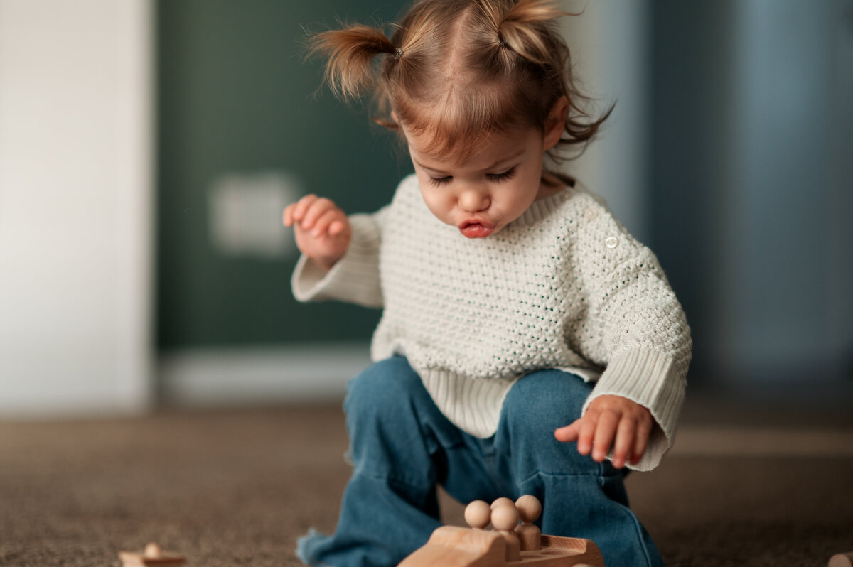 Little girl squatting on the carpet playing with wooden toys during a Story of Home session.