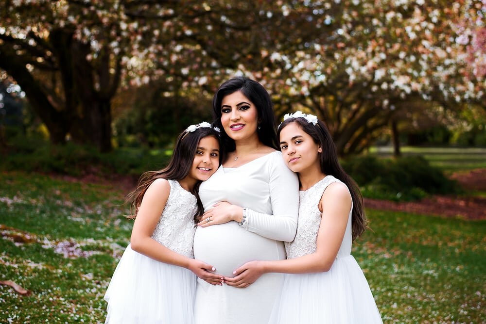 Mother and 2 daughters in white dresses  surrounded by cherry blossoms