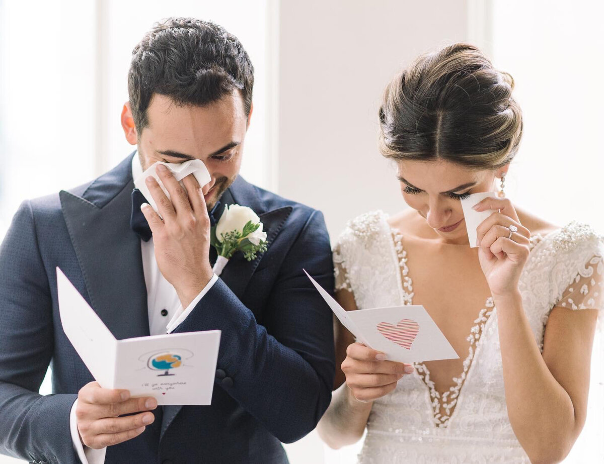 A teary couple dabs their eyes with tissue while they cry reading the cards they wrote one another on their wedding day