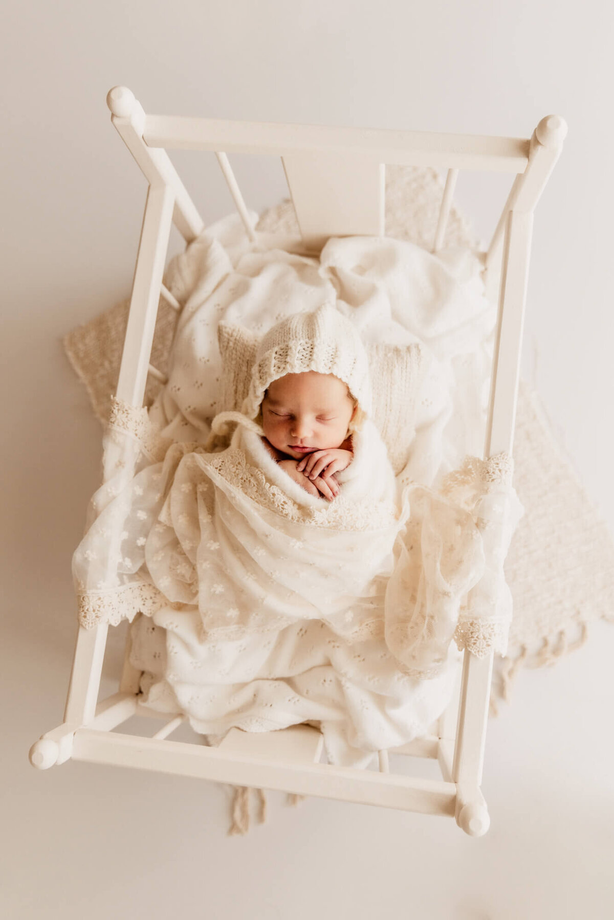 Oklahoma City baby girl sleeping in a white swaddle with her hands near her face on a white floor.