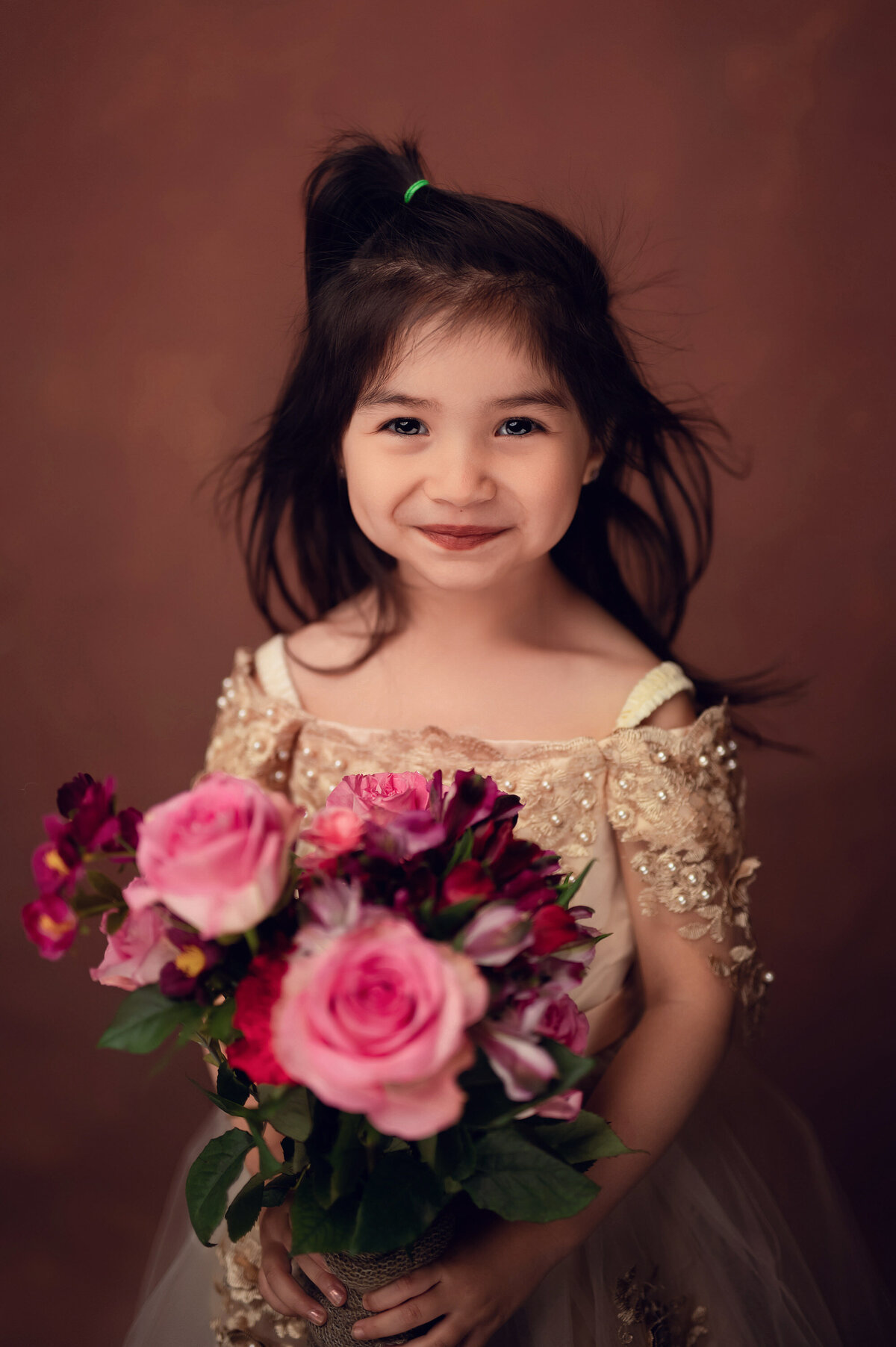 A young girl in a neutral, beaded gown holds a bouquet of pink roses in our Waukesha portrait studio.