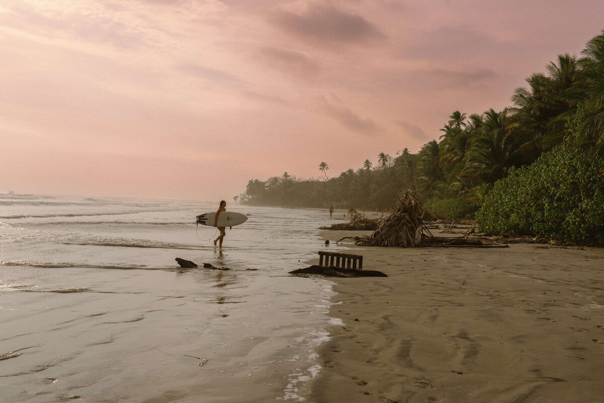 Girl walking doen the beach with surfboard