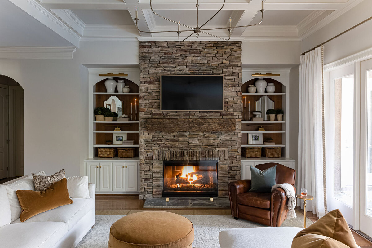 Living room with stone fireplace, white built-ins with brass fixtures and hardware, and warm accents.