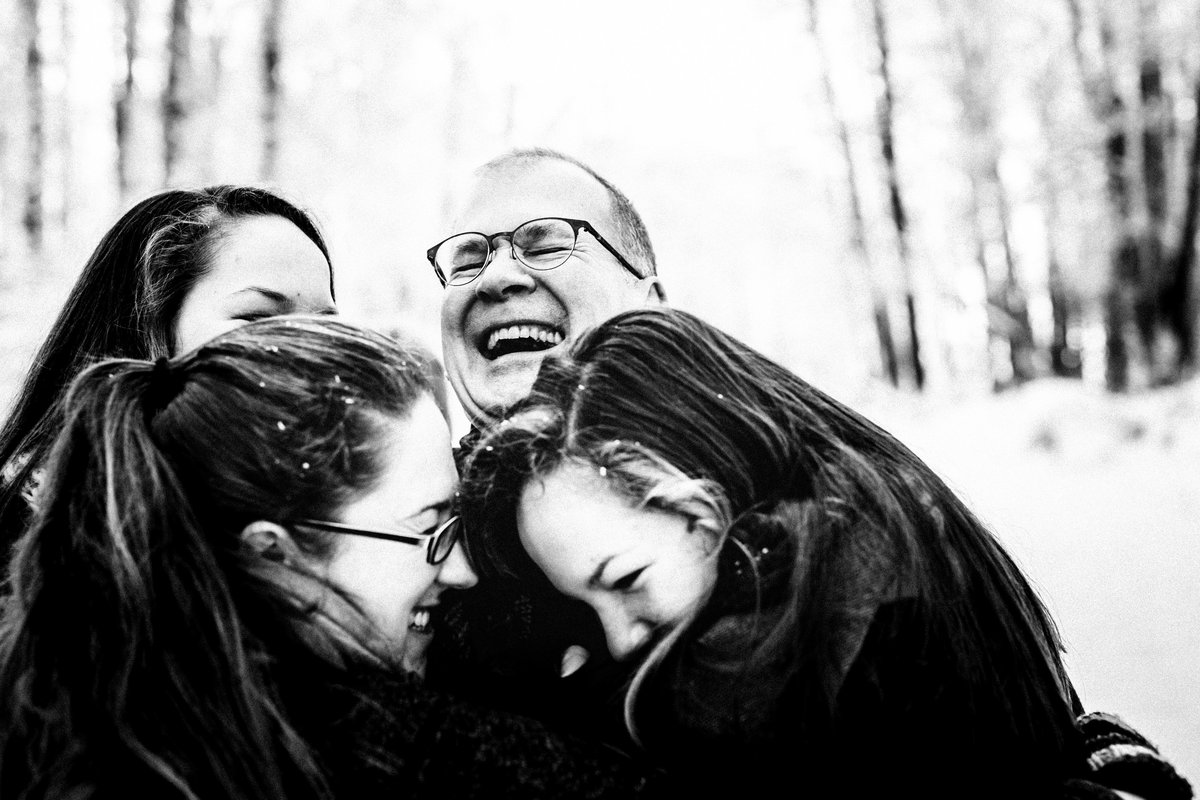 dad laughs while being hugged by daughters