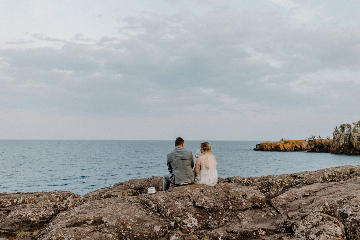 Bride and Groom sipping on juice while sitting on the rocks during their black beach MN elopement.