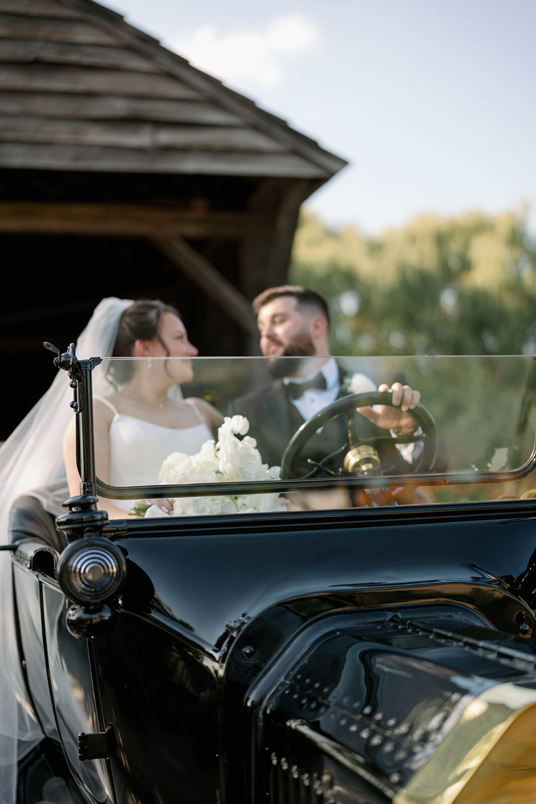 Newlyweds sitting together inside a vintage black car at Dearborn Village after their Martha-Mary Chapel ceremony.