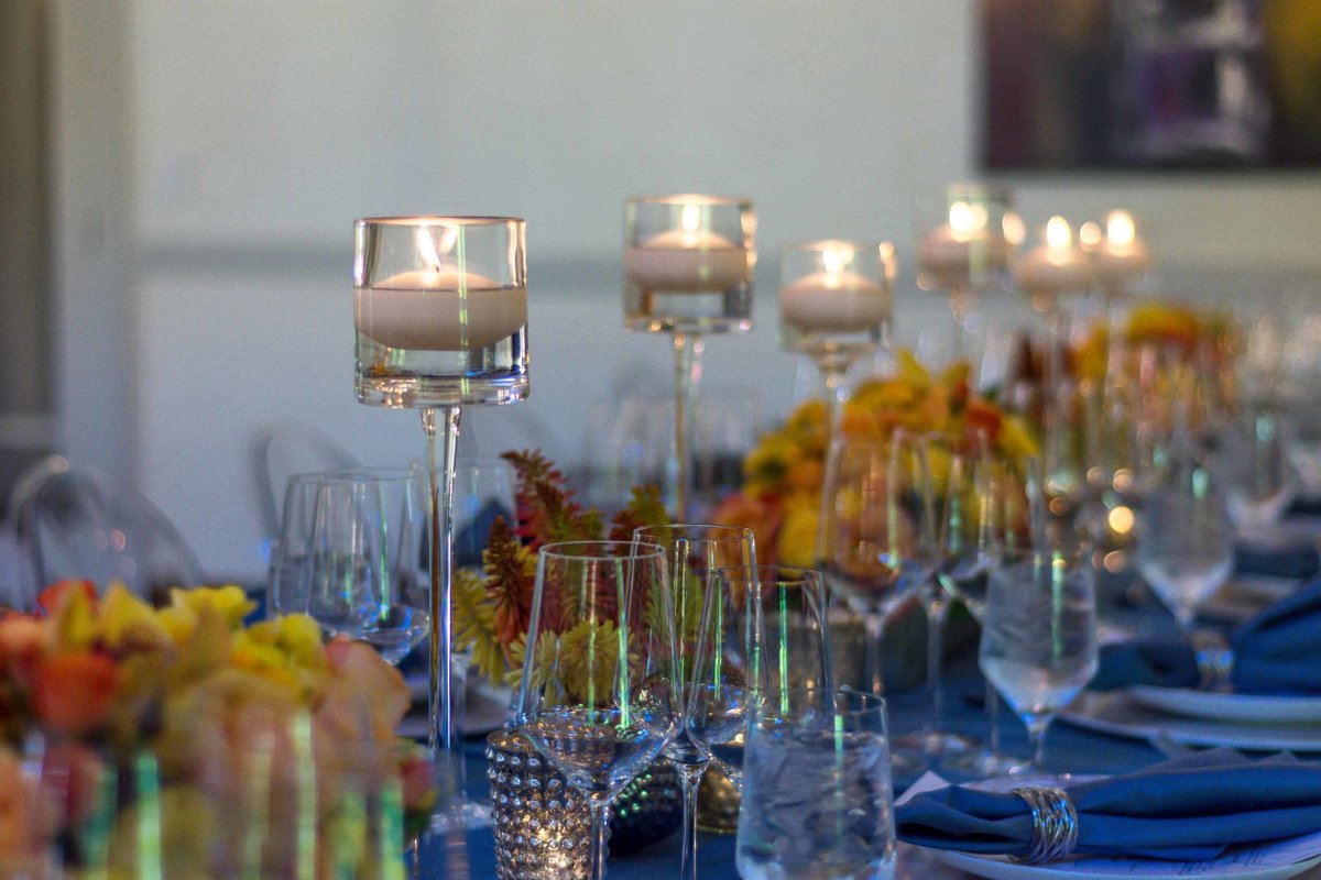 reception table with tall floating candles, orange flower centerpieces, on blue linen