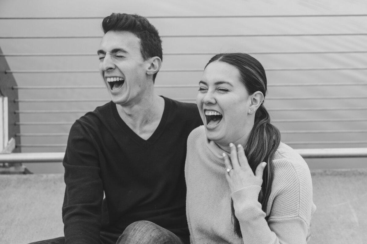 Two people smile while showing off their new engagement ring.